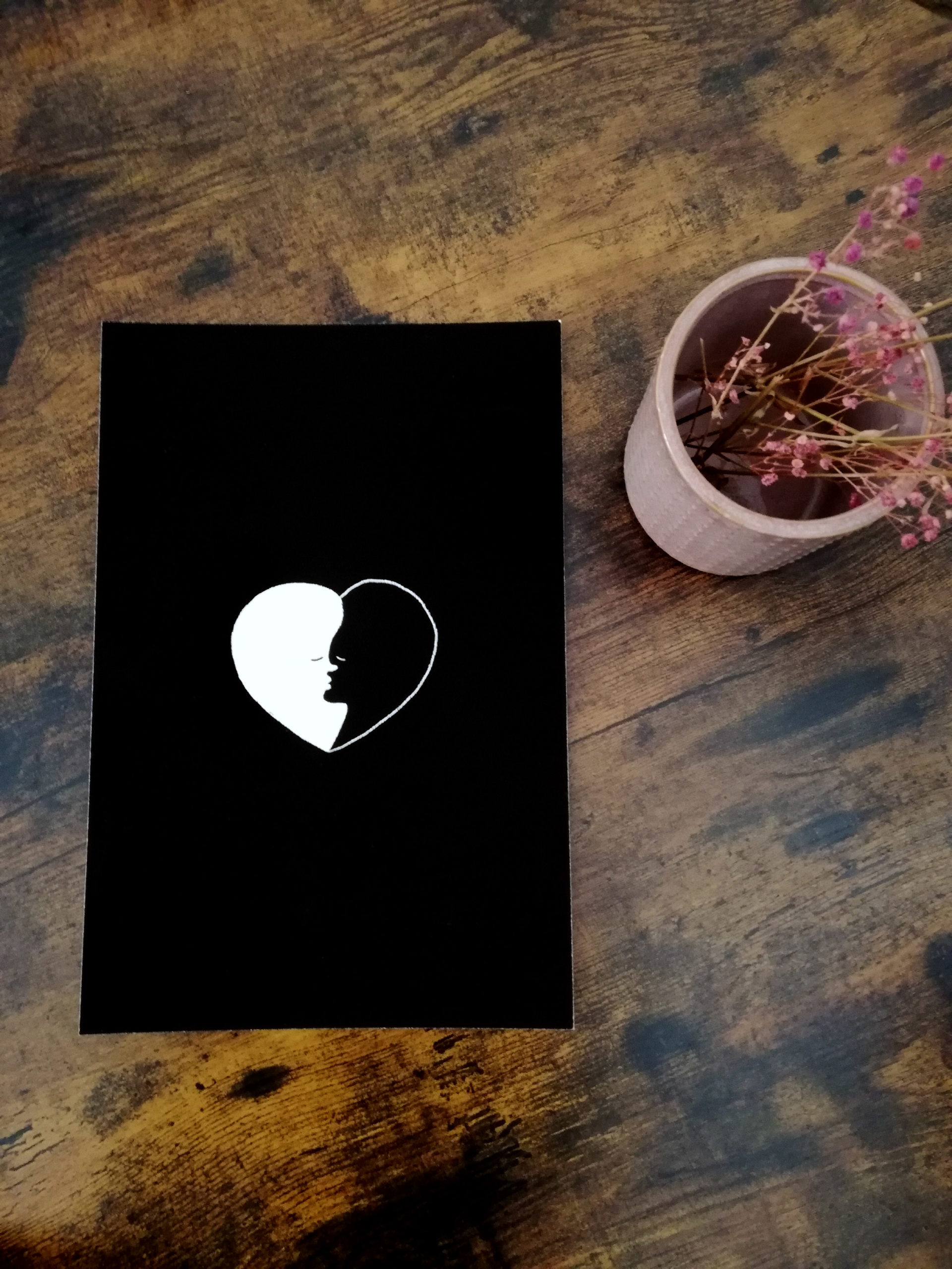 Illustration au format A4 "Yin yang love" posée sur une table à côté d'un pot de fleurs